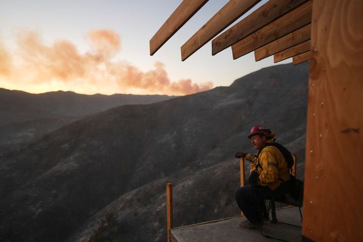 Slökkviliðsmaður kastar mæðinni eftir glímu við Palisades-eldinn við Los Angeles um helgina. Í baksýn sést reyk leggja frá eldi.