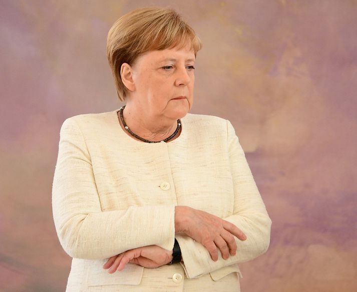 Angela Merkel sést hér halda handleggjunum þétt að sér, að því er virðist til að hafa heimil á skjálftanum.