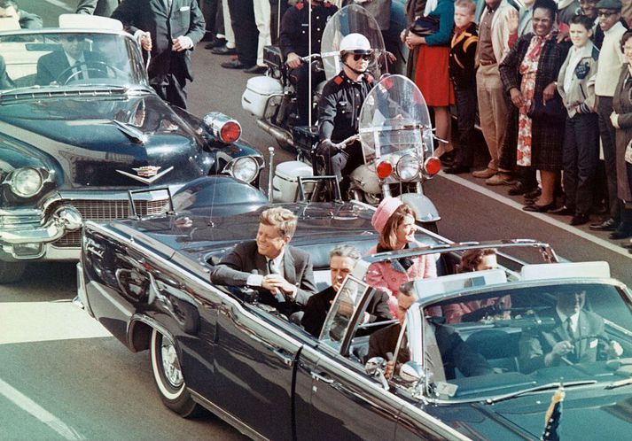 John F. Kennedy sést hér í bílalestinni ásamt eiginkonu sinni Jacqueline Kennedy. Fyrir framan forsetann situr John Connally sem særðist alverlega í skotárásinni en lifði af.