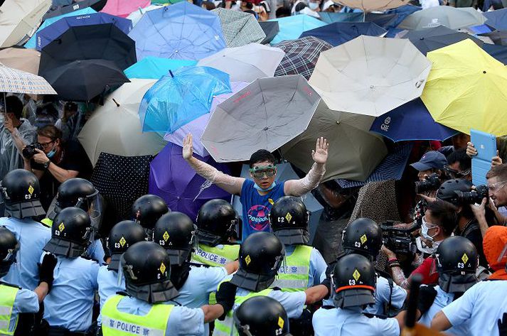 Lýðræðissinni ögrar lögreglunni fyrir framan stjórnarráðið í Hong Kong. Í bakgrunni er hópur mótmælenda með regnhlífar en þær hafa verið eins konar táknmynd mótmælanna.