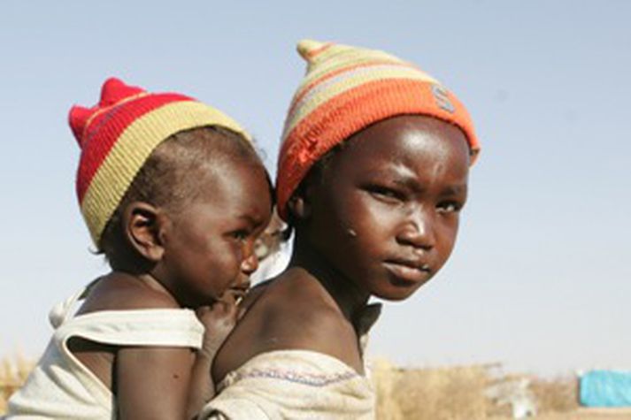 Ung stúlka ber systur sína á bakinu. Þær eru í flóttamannbúðum fyrir fólk sem hefur þurft að flýja ástandið í Darfur.