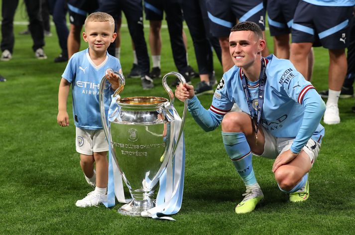 Phil Foden og Ronnie sonur hans fagna með bikarinn eftir sigur Manchester City í Meistaradeildinni.