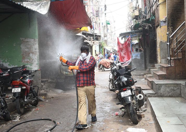 Starfsmaður borgarinnar spautar sótthreinsiefni á götur Delhi.