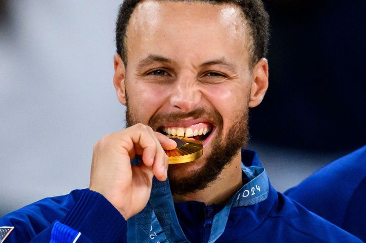 Stephen Curry bítur í gullverðlaunapeninginn sem hann vann með bandaríska landsliðinu á Ólympíuleikunum í París á dögunum.