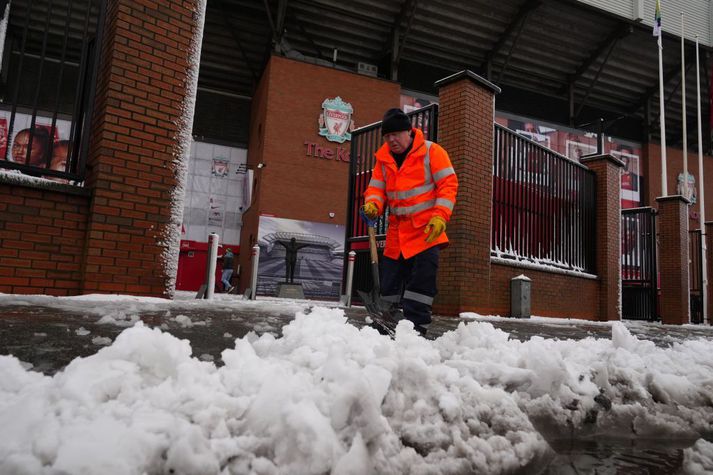 Mikil snjókoma hefur valdið ýmsum vandræðum á Englandi. Hér hreinsar starfsmaður á Anfield stéttina.