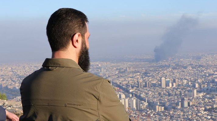 Hér má sjá Ahmed Hussein al-Sharaa, leiðtoga HTS-samtakanna í Sýrlandi, virða fyrir sér Damaskus-borg og það reykjarmökk sem talinn er vera vegna loftárásar Ísraela í morgun. Hann hefur lengi gengið undir nafninu Abu Mohammed al-Jolani en opinberaði raunverulegt nafn sitt á dögunum.