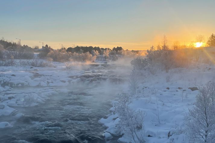 Ísþoka stígur upp af Elliðaám ofan Vatnsveitubrúar. Sólin rétt gægist upp fyrir sjóndeildarhringinn.