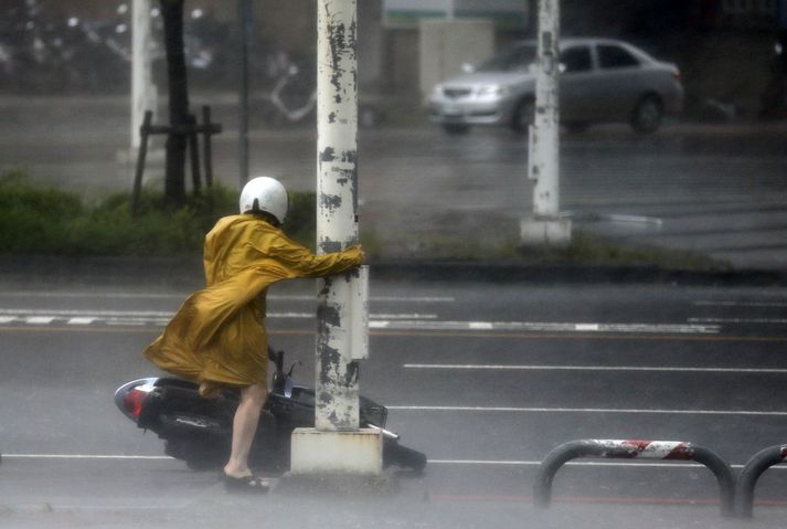 Kona rígheldur í ljósastaur til að fjúka ekki.